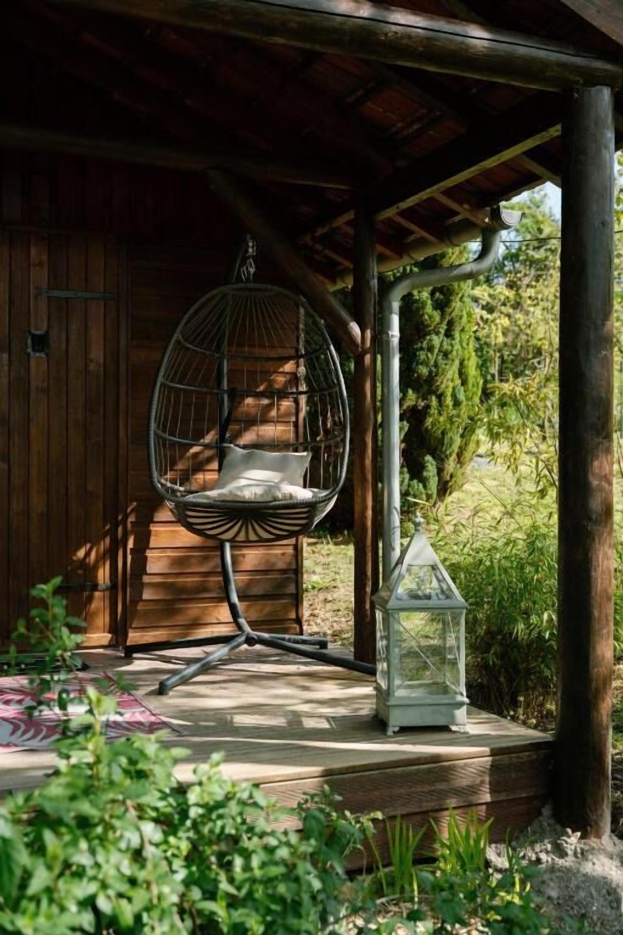 Uma cabana de madeira com uma cadeira suspensa e um candeeiro numa varanda de madeira.