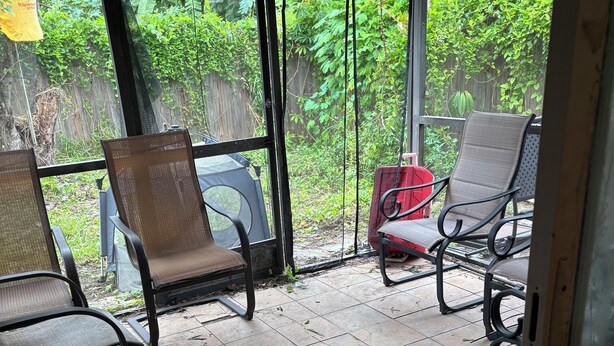 A covered outdoor seating area with chairs and a table, surrounded by a wooden fence and lush greenery. - The Single Vacation Rental Dwelling (Orlando)