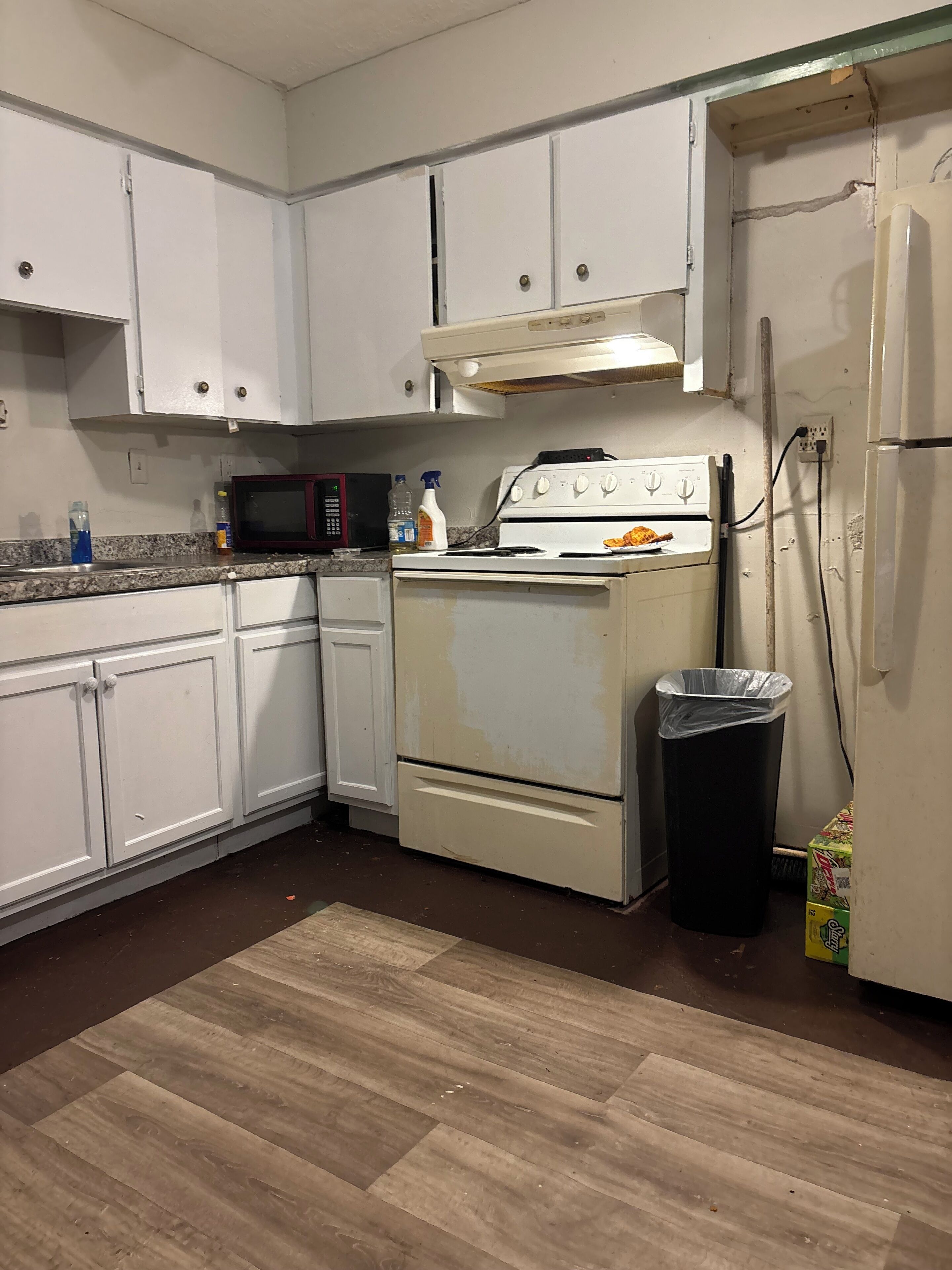 A kitchen with white cabinets, a microwave, a stove, and a trash can.