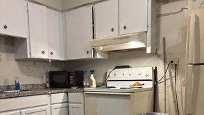 A kitchen with white cabinets, a microwave, a stove, and a trash can. - The Single Vacation Rental Dwelling (Orlando)