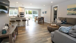 Un salon moderne avec un canapé gris, un plancher en bois et un coin repas comprenant une table et des chaises.
