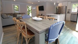 Une cuisine moderne avec des meubles blancs, un réfrigérateur en acier inoxydable et un coin repas comprenant une table et des chaises en bois.