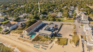 Vue aérienne d’un hôtel situé sur la côte, avec une piscine, des chaises longues sur la plage et un parking.