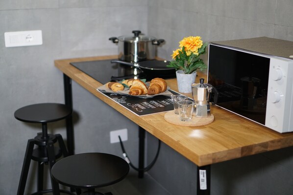 Un comptoir de cuisine avec un four à micro-ondes, une casserole sur la cuisinière et une assiette de croissants. Il y a deux tabourets et une petite table.