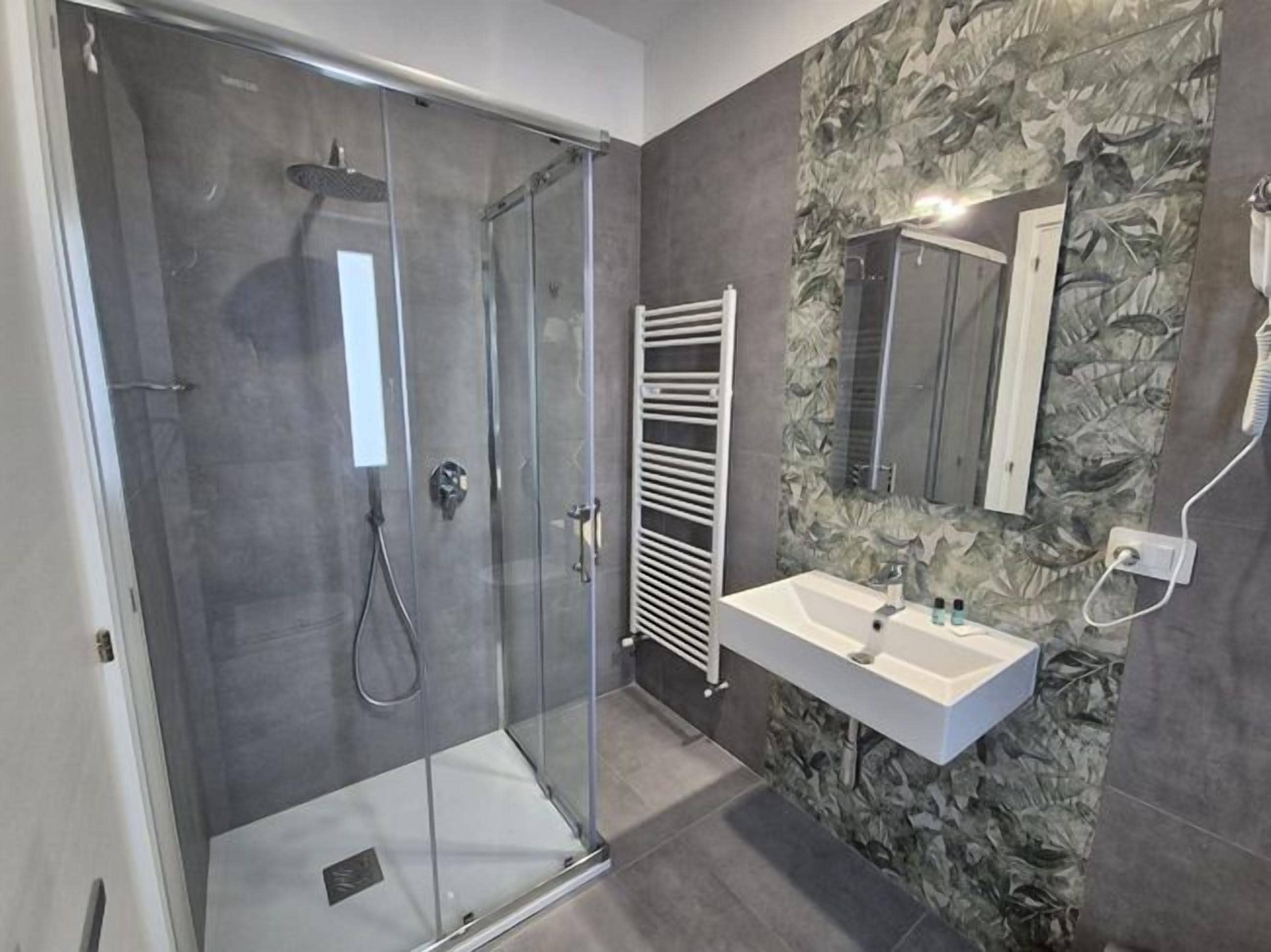 Ein modernes Badezimmer mit einer in Glas abgeschirmten Dusche, einem weißen Waschbecken und einem wandmontierten Spiegel.