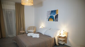 Un lit bien fait, recouvert d’une couverture marron, une chaise en osier, une table de chevet avec une lampe et une œuvre d’art accrochée au mur.