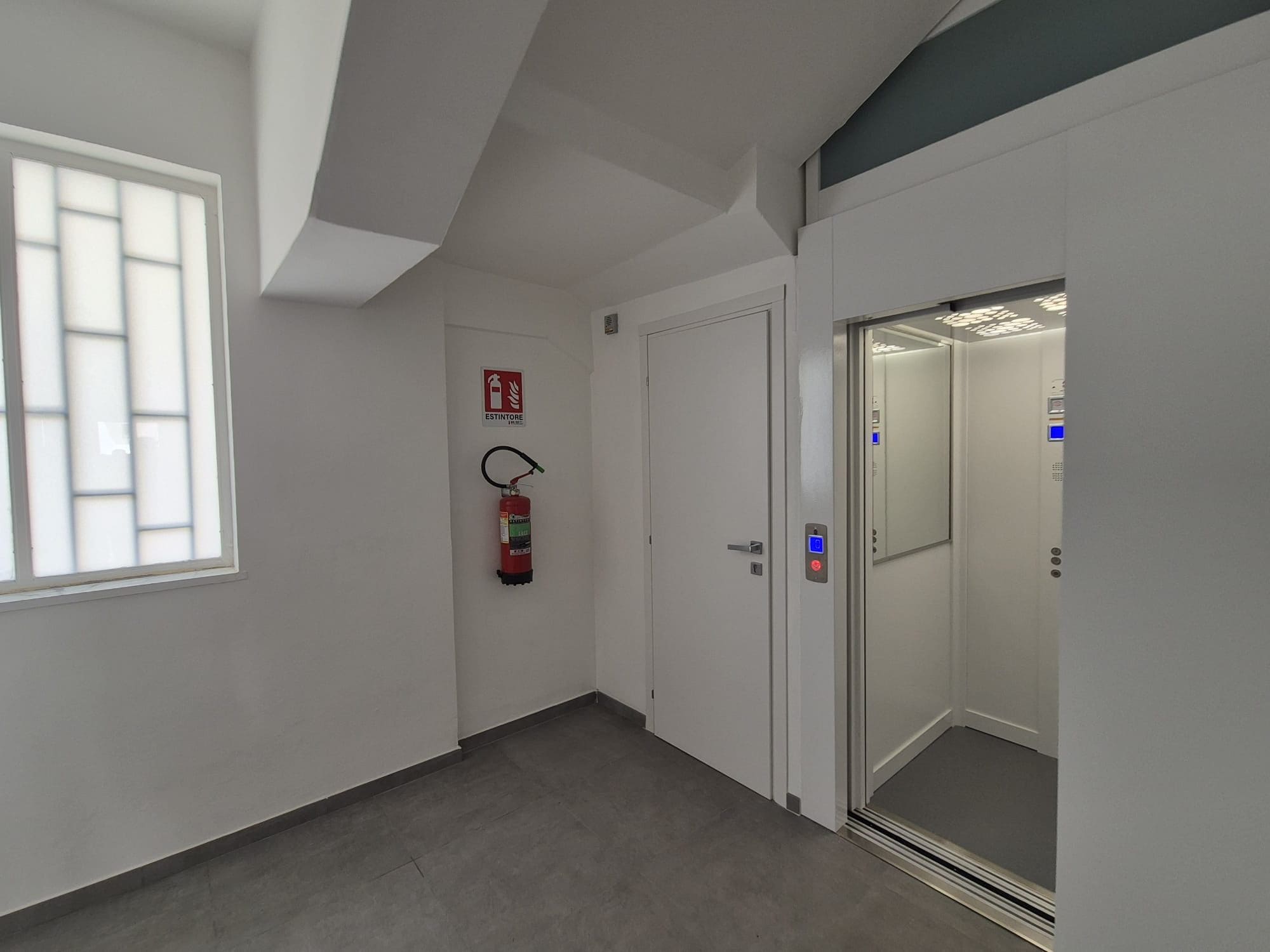 A hallway with a fire extinguisher, a door, and an elevator.