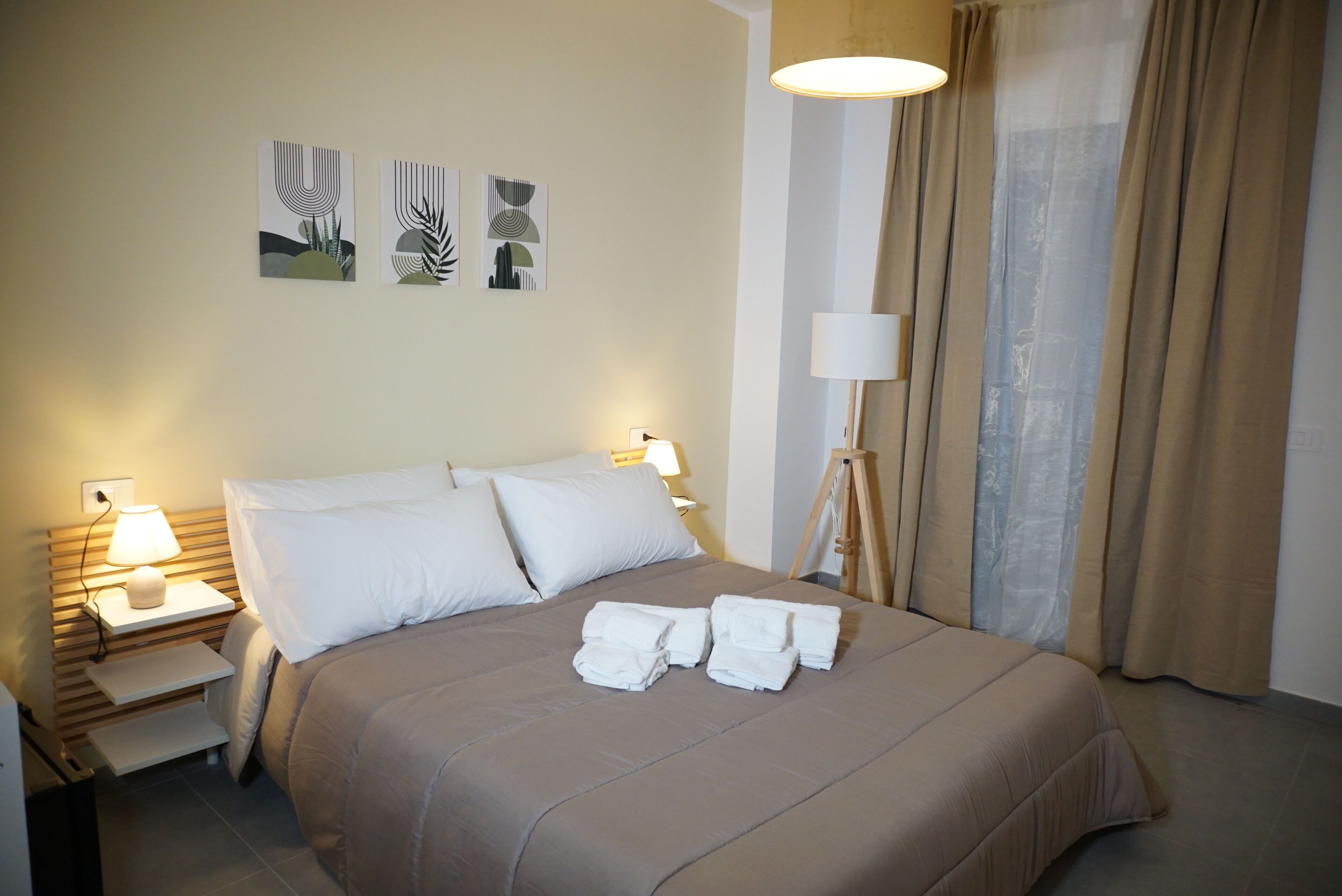 A neatly made bed with white linens and towels, a bedside lamp, and abstract wall art.