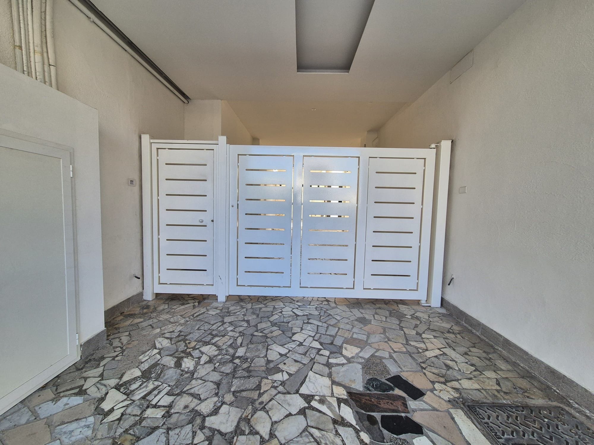 A hallway with a stone-tiled floor and a white gate with horizontal slats.