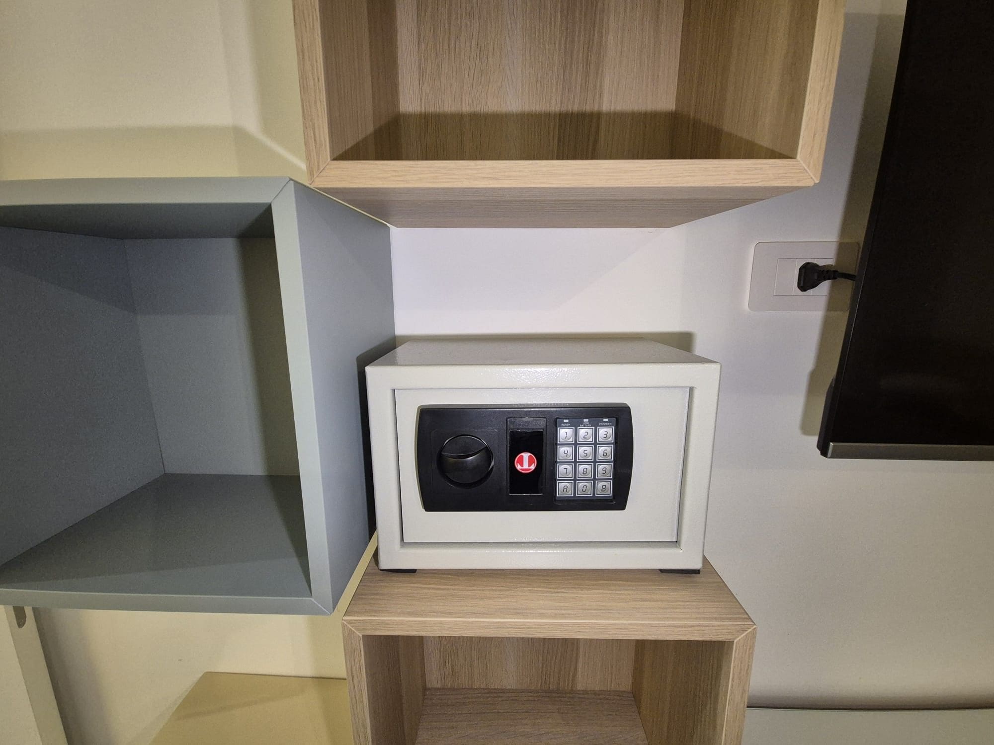 Un four à micro-ondes blanc est posé sur une étagère en bois, dans un coin d’une pièce. Un meuble en bois se trouve au-dessus.