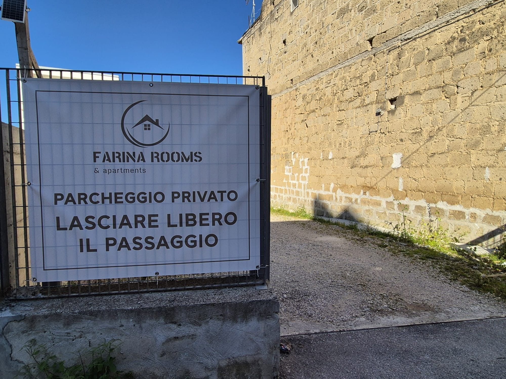 Placa indicando 'Farina Rooms & apartments', com área de estacionamento privativo e uma passagem.