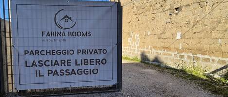Placa indicando 'Farina Rooms & apartments', com área de estacionamento privativo e uma passagem.