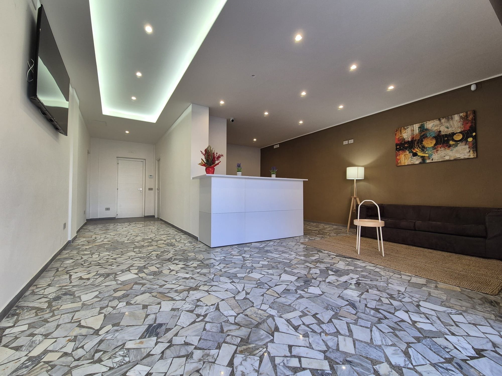 Uma área de recepção com piso de ladrilho de pedra, balcão de recepção branco, sofá e um quadro na parede.