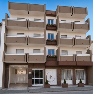 Un immeuble résidentiel à plusieurs étages, doté de balcons, d’une entrée sécurisée et d’une enseigne indiquant « IRINA ROOMS ».