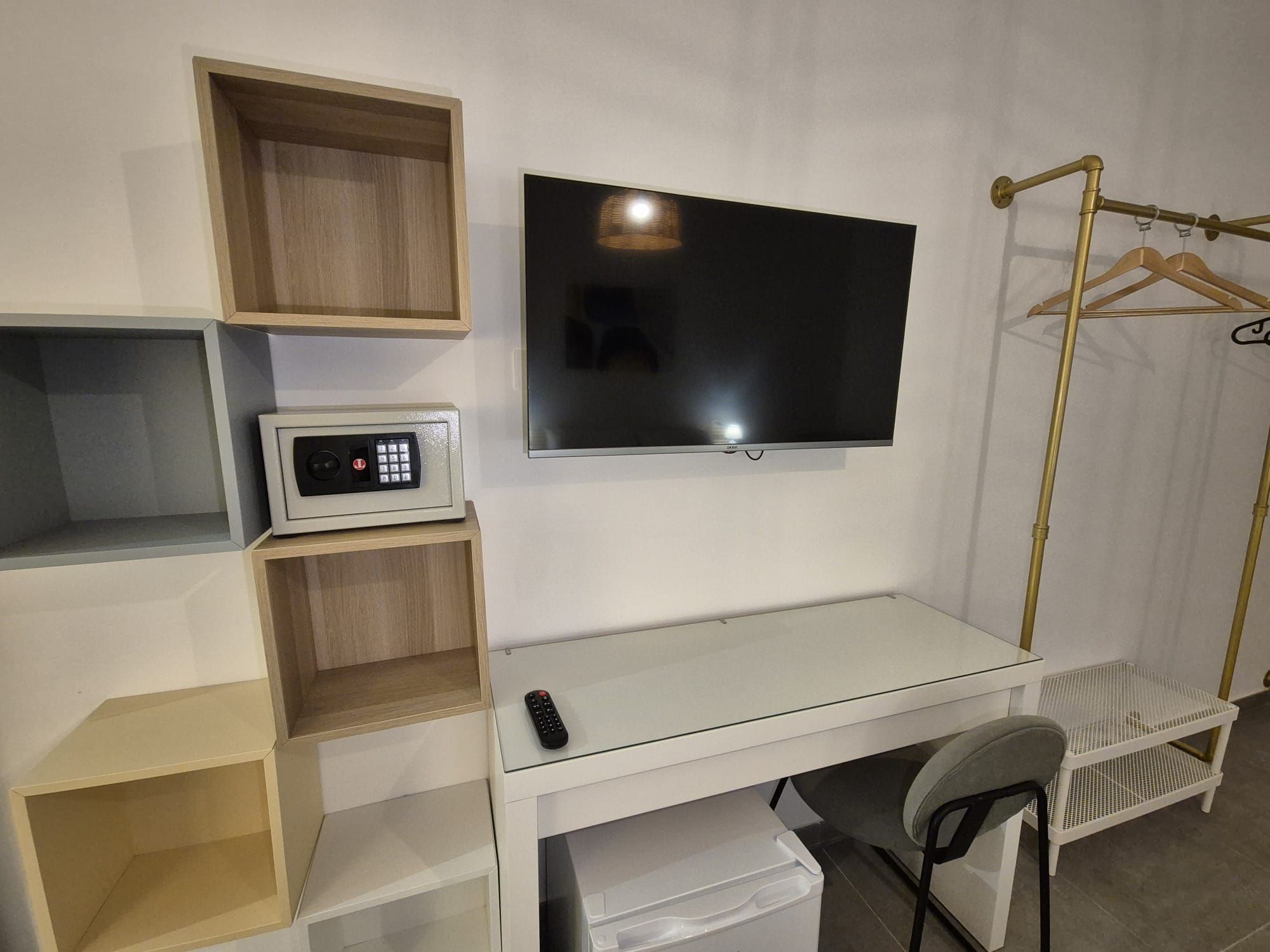Une chambre compacte équipée d’un téléviseur fixé au mur, d’un four à micro-ondes, d’un petit bureau avec une chaise et d’un porte-vêtements.