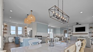 A modern kitchen with white cabinetry, a central island, and pendant lighting. - Silver Lining- Luxury Retreat in Dolphin Ridge (Emerald Isle)
