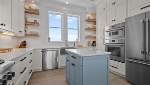 A modern kitchen with white cabinetry, stainless steel appliances, and a blue island. - Silver Lining- Luxury Retreat in Dolphin Ridge (Emerald Isle)