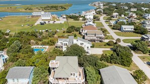 A residential area with houses, a swimming pool, and a large body of water in the background. - The Bedloe: Cozy Beach Cottage (Emerald Isle)