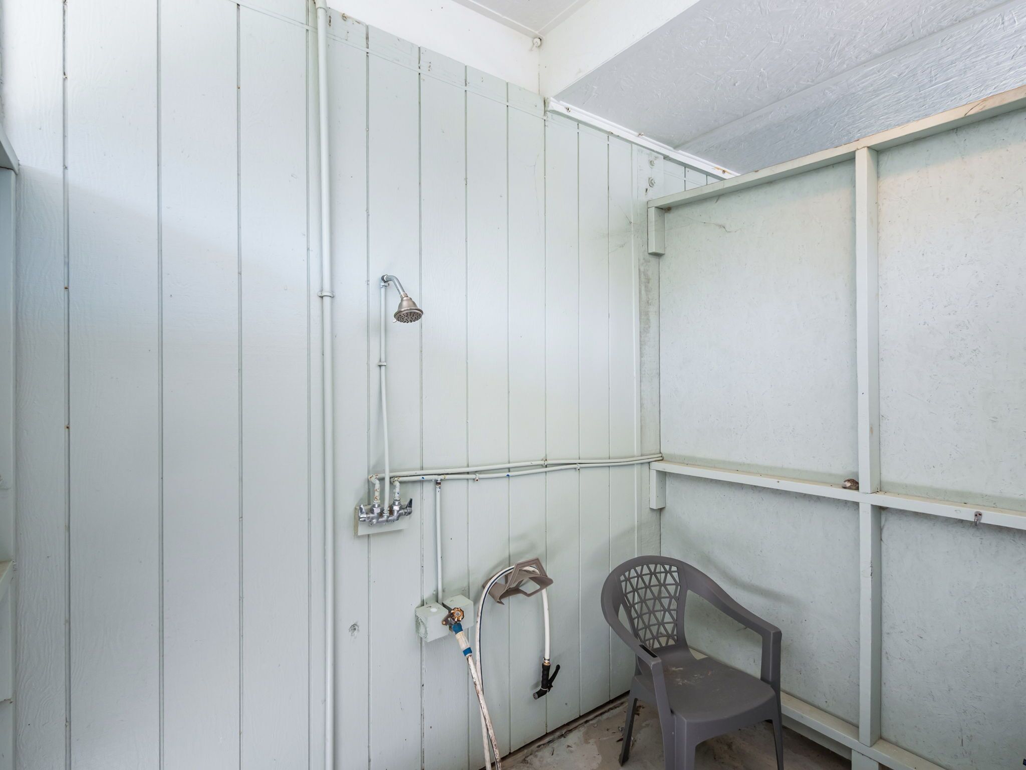 A bathroom with a shower, a toilet, and a chair.