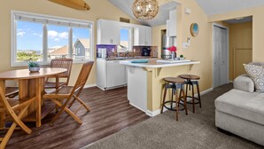 A modern kitchen with white cabinets, a central island, and a view of the beach. - The Bedloe: Cozy Beach Cottage (Emerald Isle)