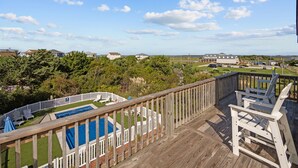 A wooden deck with a pool, lounge chairs, and a view of a residential area. - The Jackson: Cozy Beach Cottage with Pool! (Emerald Isle)