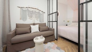 Ein modernes Schlafzimmer mit einem braunen Sofa, einem kleinen weißen Tisch, einem Bett mit rosa Bettdecke und einem großen Fenster mit Aussicht.