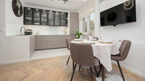 Eine moderne Küche mit integriertem Backofen, einem Essbereich mit Tisch für zwei Personen und einem an der Wand montierten Flachbildfernseher.