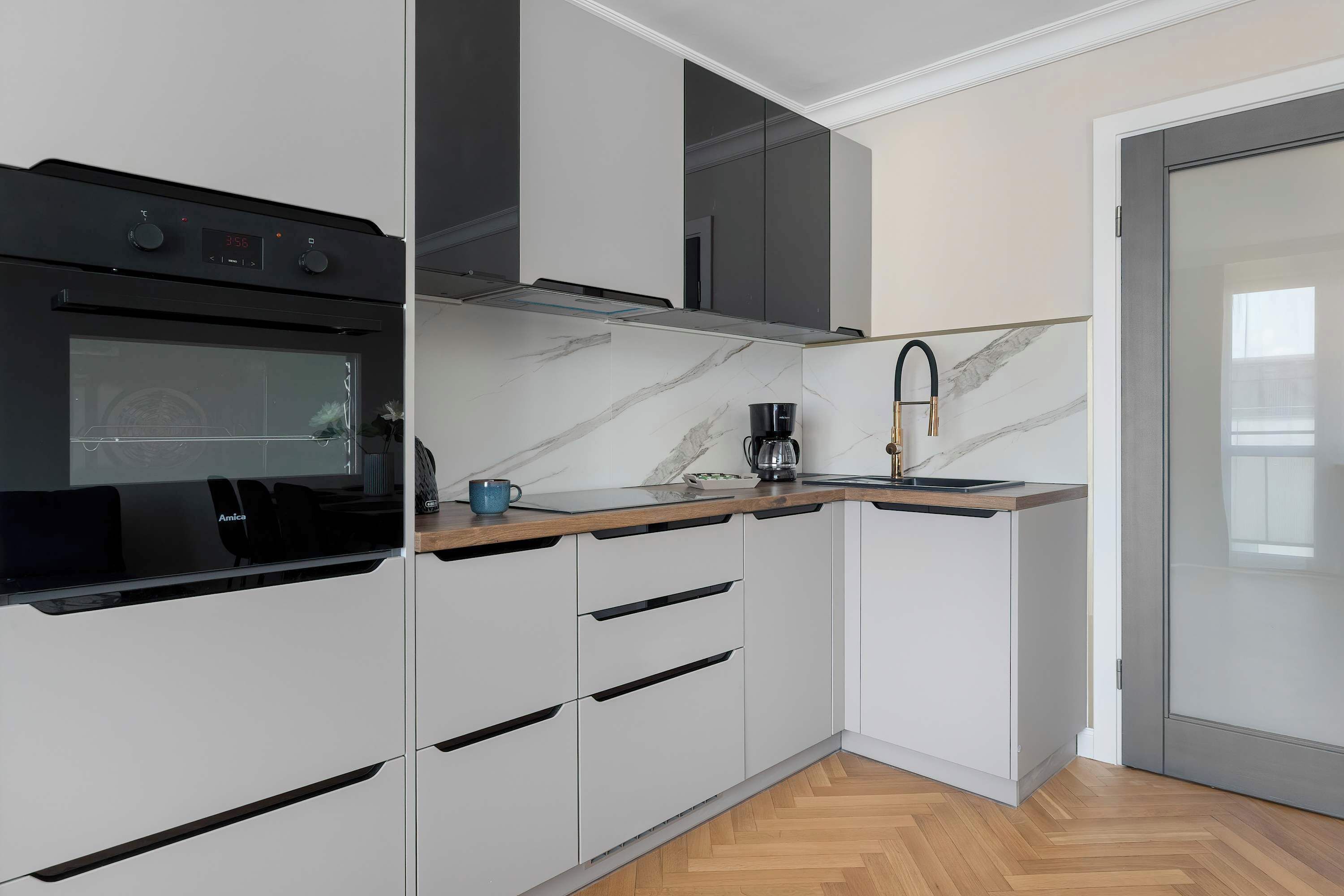 Una cocina moderna con armarios blancos, un horno negro, encimera de mármol y una cafetera.