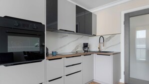 Una cocina moderna con armarios blancos, un horno negro, encimera de mármol y una cafetera.