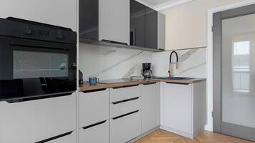 Una cocina moderna con armarios blancos, un horno negro, encimera de mármol y una cafetera.