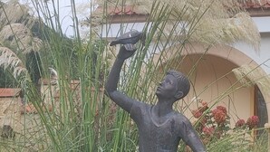 Un jardín con una estatua, hierbas altas y flores.
