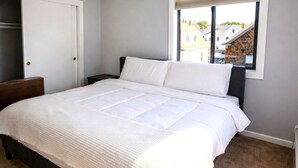 Ein Schlafzimmer mit einem großen Bett, einem Fenster mit Blick auf Gebäude und einer Tür zu einem Schrank.