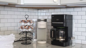 Eine Küche mit weißen Schränken, einer Kaffeemaschine, einem Keurig-Kapselspender und Salz- und Pfefferstreuern.