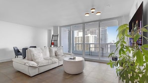 Un salon moderne avec un canapé blanc, une table basse ronde et une grande fenêtre donnant sur la ville.