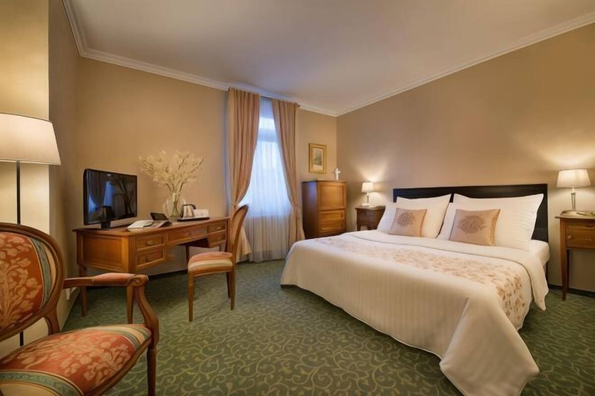 A hotel room with a bed, a desk, a chair, a television, and a lamp.