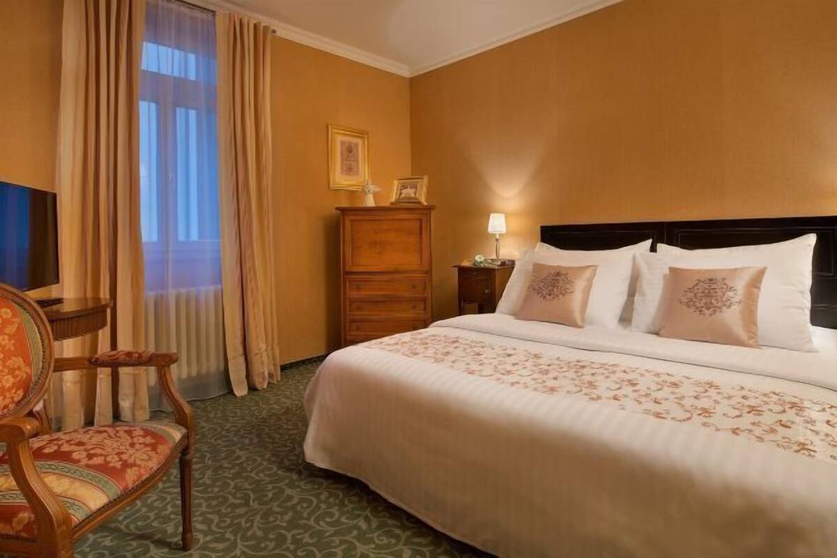 A hotel room with a bed, a chair, a dresser, and a television.