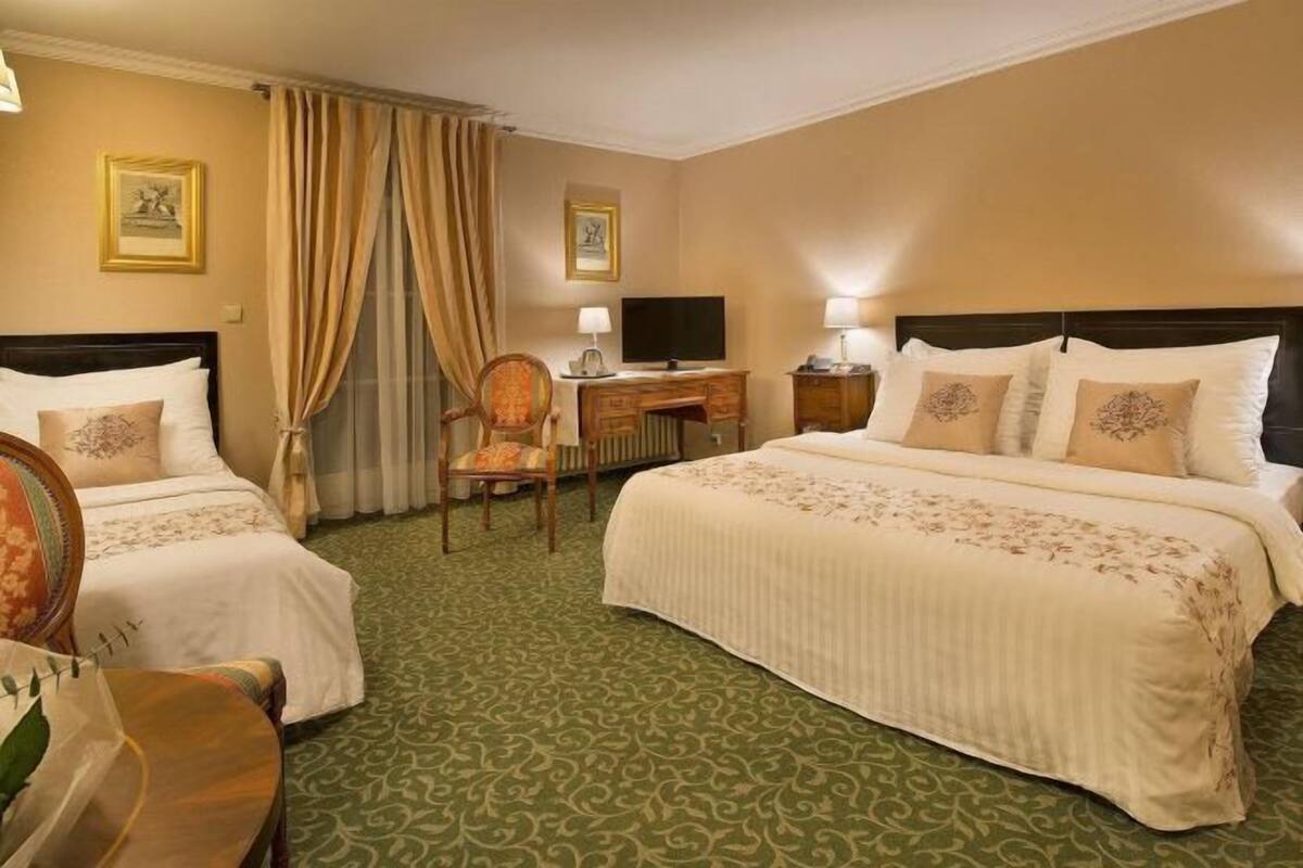 A hotel room with two beds, a desk, a chair, and a television.