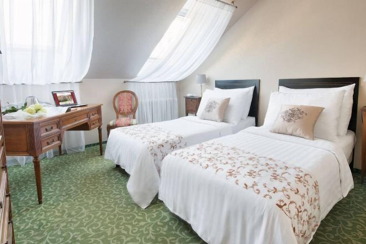 A hotel room with two beds, a desk, a chair, and a window with curtains.