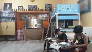 Une chambre avec un lit superposé, un bureau avec des livres et des documents, une télévision et des tableaux encadrés accrochés au mur.