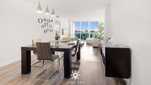 Un comedor moderno con una mesa y sillas de madera oscura, luces colgantes y vistas de la ciudad a través de amplios ventanales.
