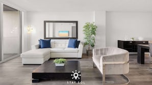 Una sala de estar moderna con un sofá blanco, una mesa de centro con una planta, un espejo grande y un comedor con una mesa y sillas negras.
