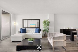 Una sala de estar moderna con un sofá seccional, una mesa de centro, un sillón, un espejo grande y una planta en maceta.
