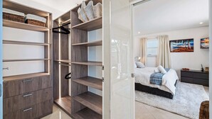 Une chambre à coucher moderne, comprenant un lit, une table de chevet, une commode et un dressing avec des étagères et un espace pour suspendre les vêtements.