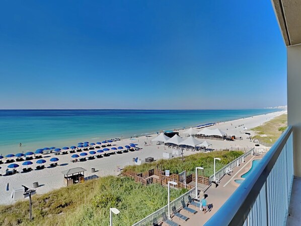 A beach view with umbrellas, a pool, and a boardwalk.