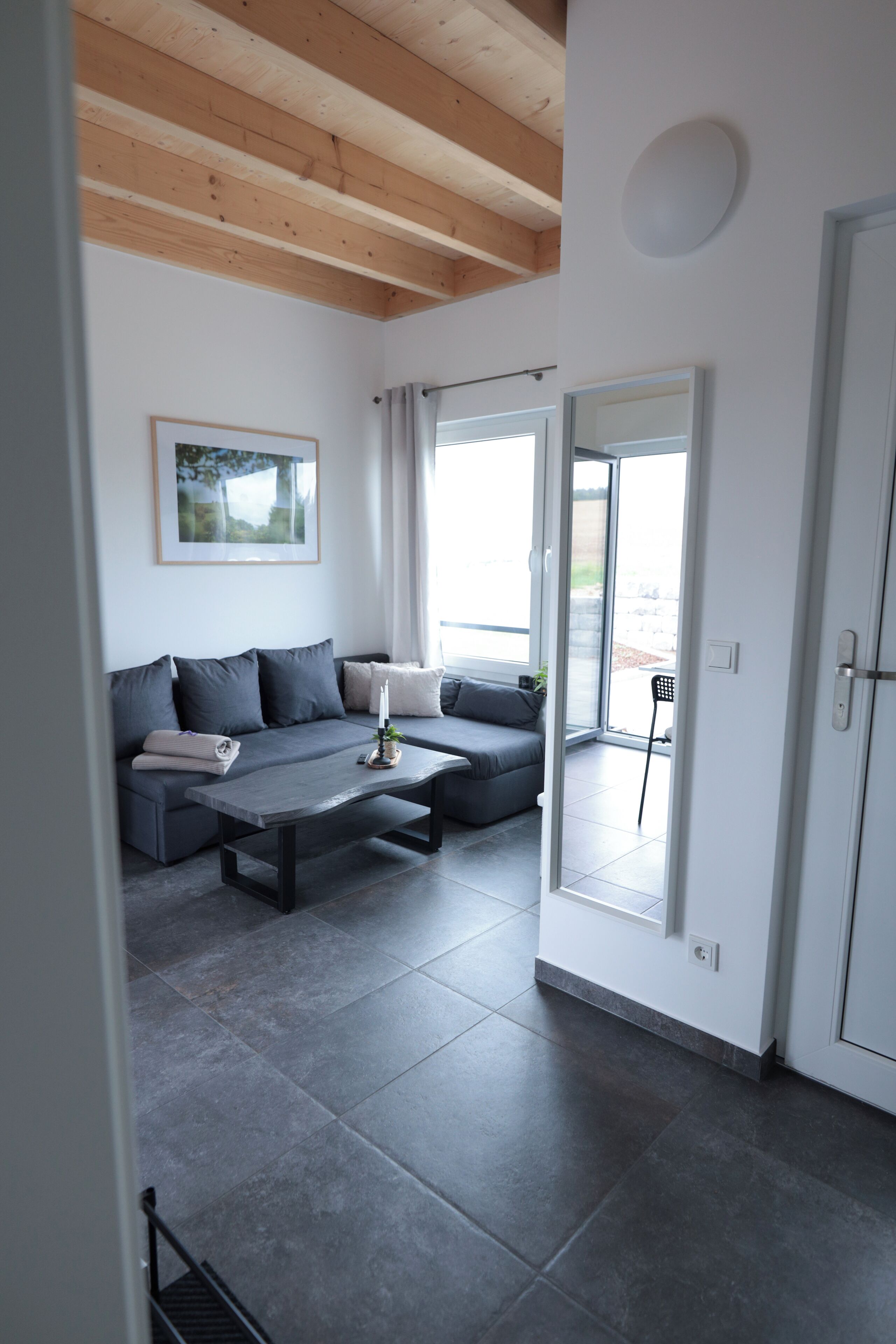 A modern living room with a grey sofa, a coffee table, and a large window.