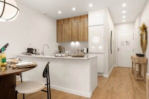 Une cuisine moderne avec des meubles blancs, un îlot central et un coin repas comprenant une table et des chaises.