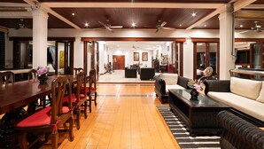 A spacious living area with a wooden dining table, chairs, and a sofa. There are ceiling fans and a television in the background. - Lumaya Rawai (Rawai)