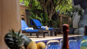 A pool area with lounge chairs, a table with bottles, and tropical plants. - Lumaya Rawai (Rawai)
