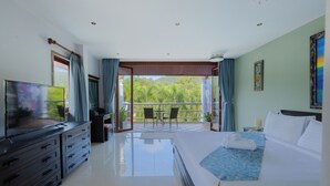 A hotel room with a bed, a TV, a dresser, and a balcony with a view of greenery. - Lumaya Rawai (Rawai)