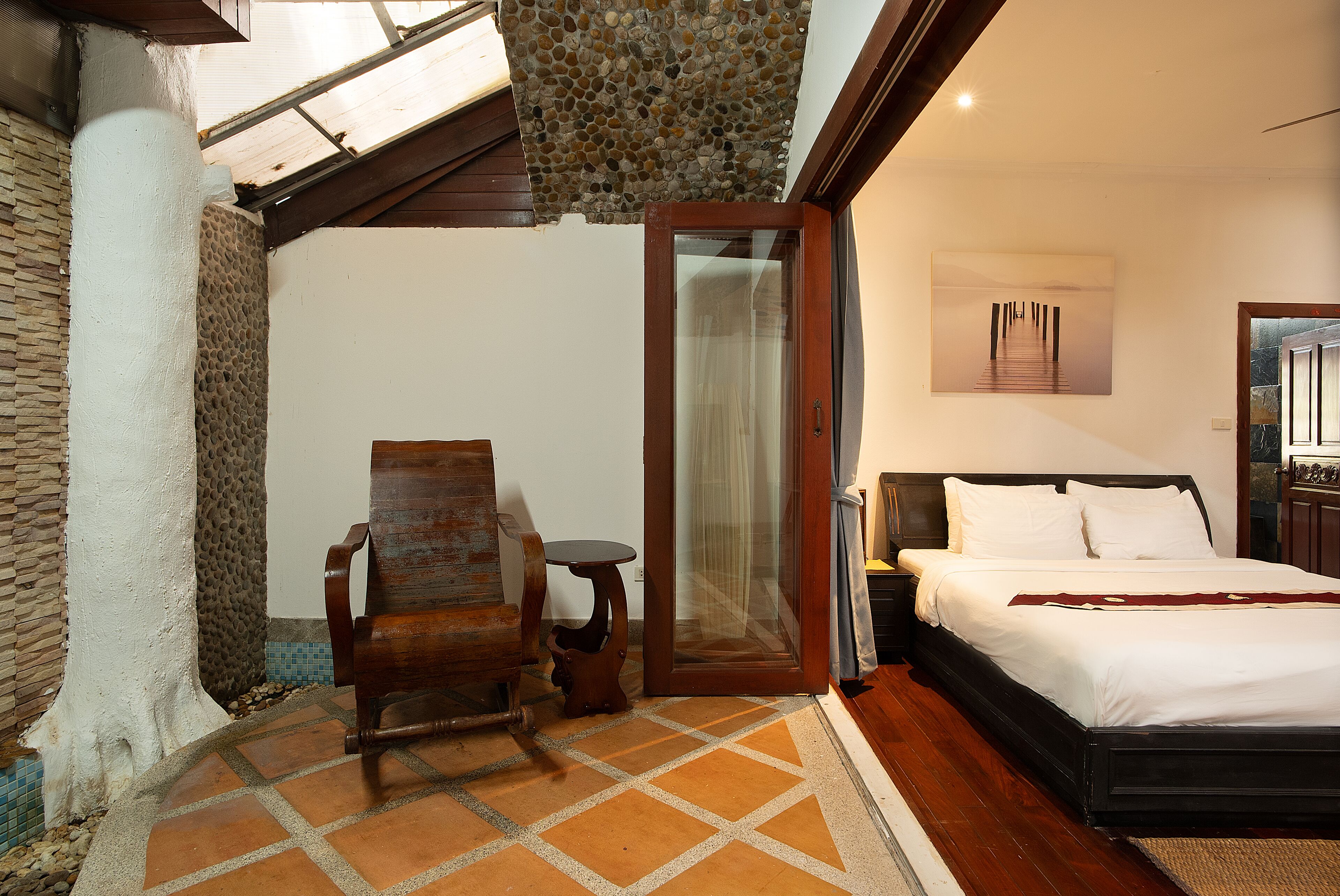 A bedroom with a bed, a chair, a small table, and a glass door leading to a balcony.